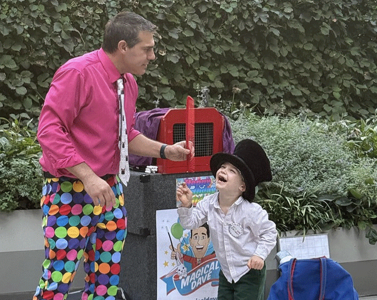 magical-dave-nyc-magic-shows-kids4 Magical Dave laughing with a young boy in a top hat during an outdoor magic show